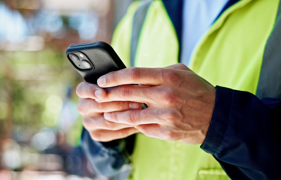 Servicetechniker mit Warnweste und Smartphone in beiden Händen